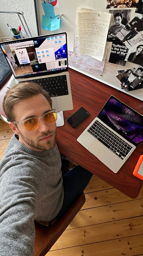 Man at a desk with two laptops wearing Skopos amber focus glasses